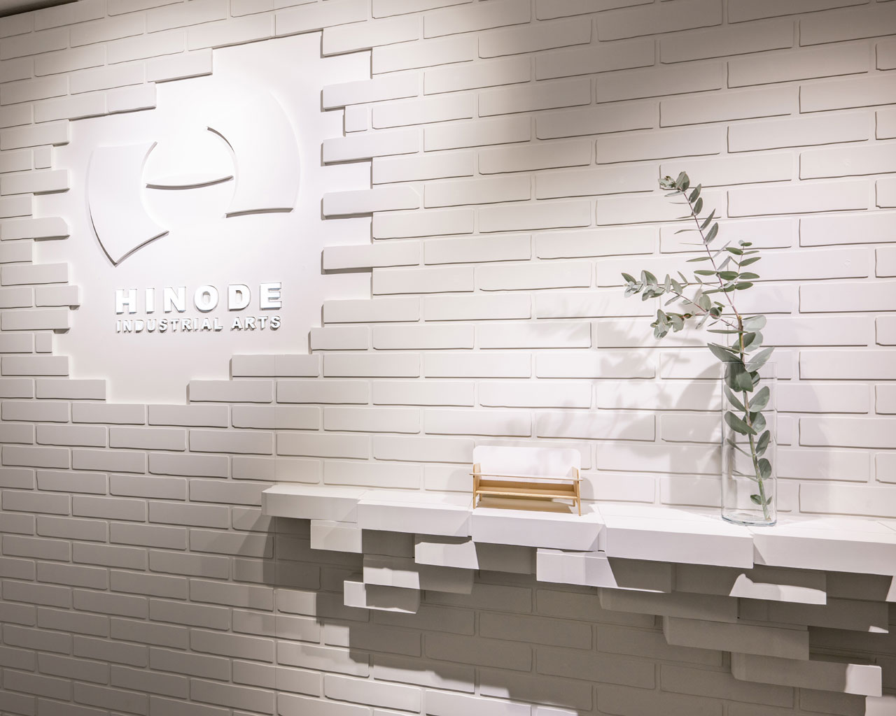 ショールームのエントランス。白のタイル壁面に、立体的なロゴサインと棚を組み合わせた「5D Wall BRICKS」による空間デザイン