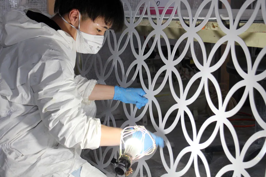 円形パターンのアルミアートパネル研磨。作業服を着用した職人による、幾何学模様の細部に至る研磨仕上げ作業