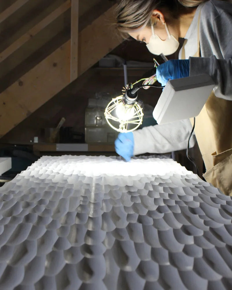 パネルの照明下での研磨作業。作業灯を使用した精密な表面研磨により、均一な質感を実現する工程